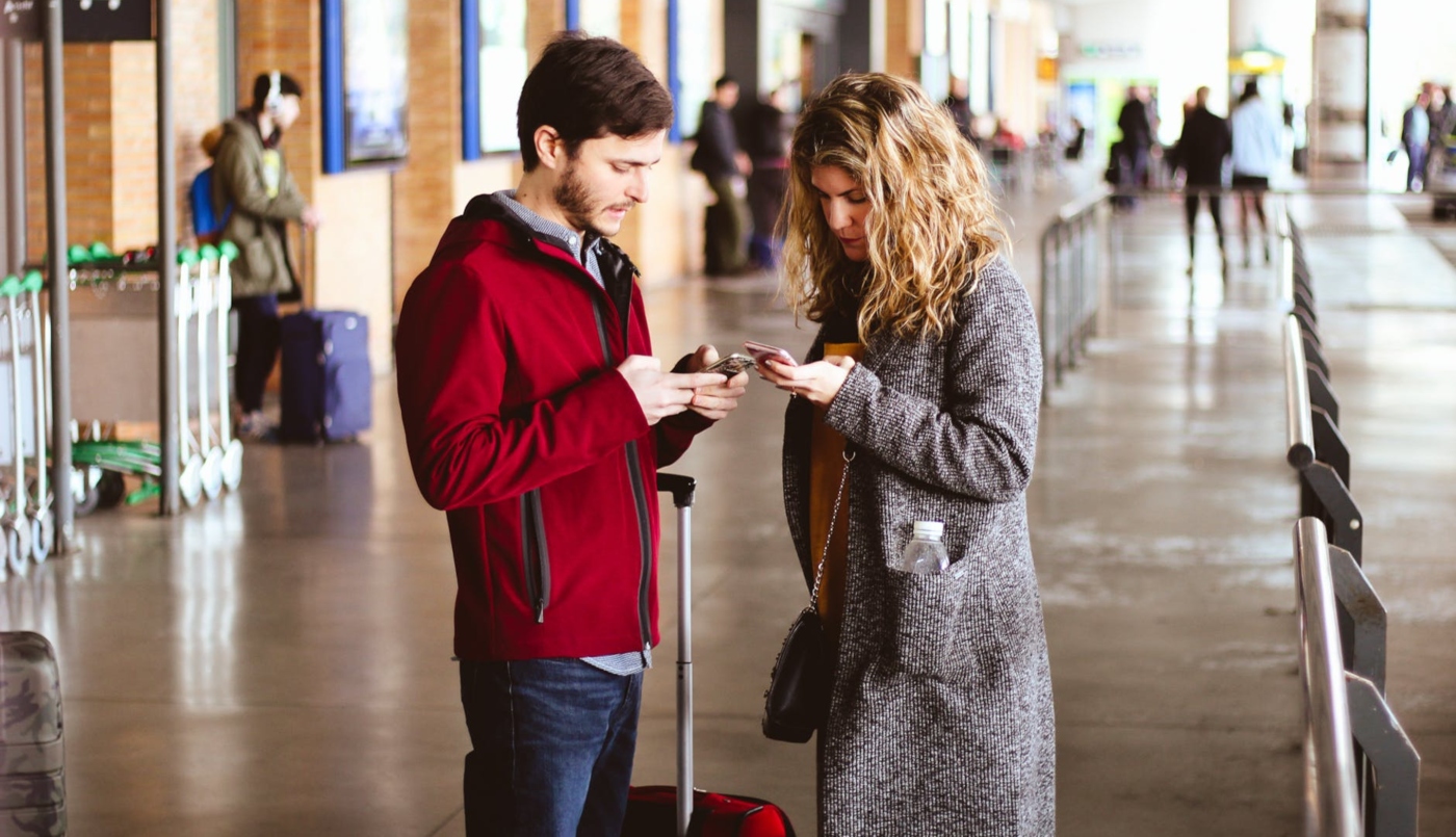 Imagen de una pareja de turistas en el aeropuerto mirando su celular 